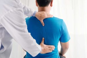 A chiropractor performing a spinal adjustment on a patient lying face down in a calm, sunlit treatment room.